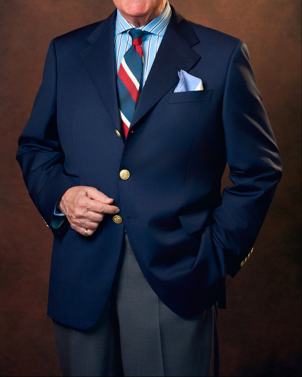 Man in a navy suit with a red, white, and blue tie against a brown background