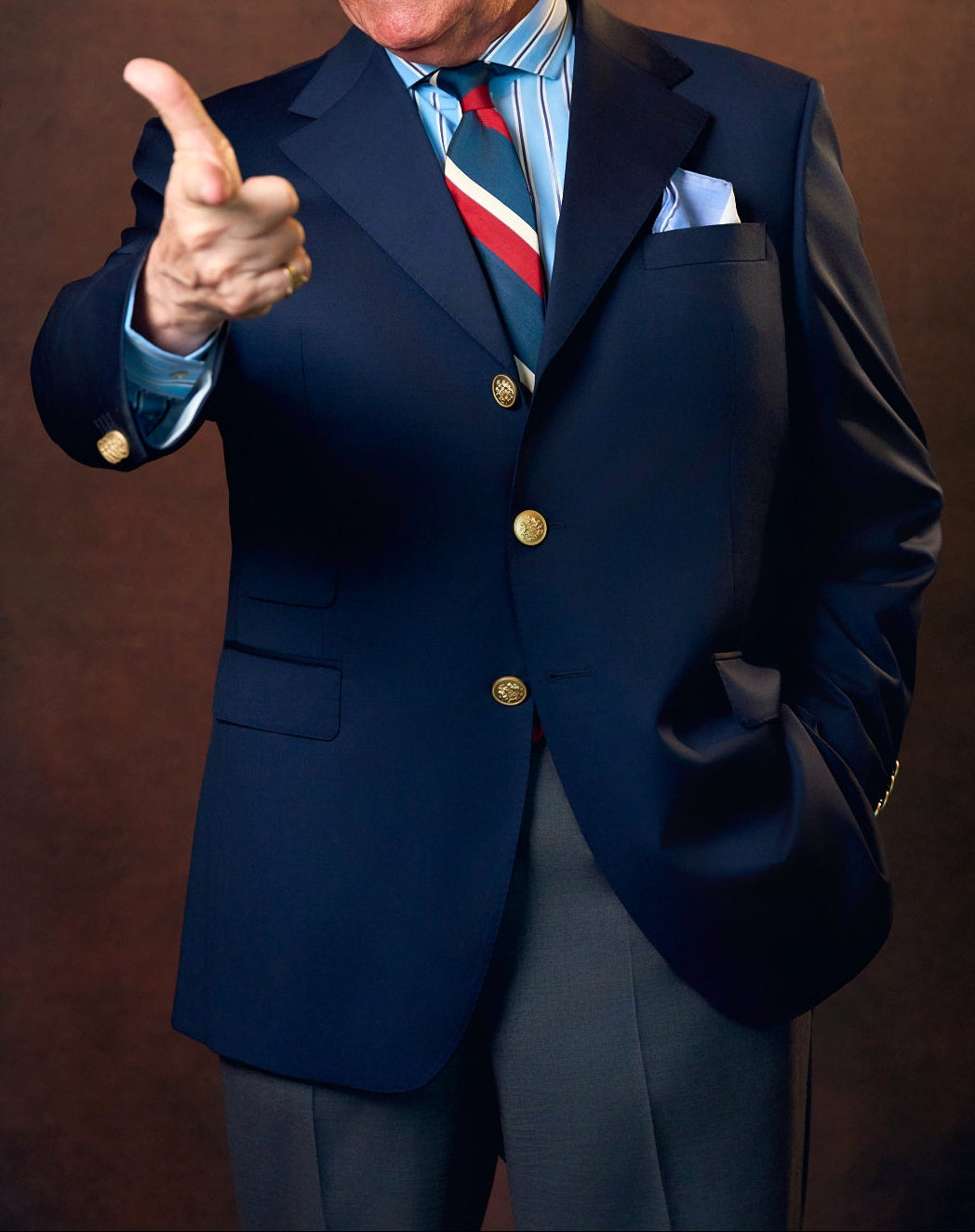 Man in a suit pointing forward against a brown background
